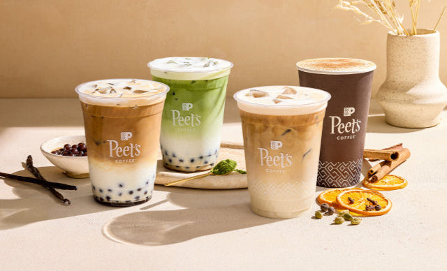 Four Peet's Coffee cups on a table with various coffee ingredients.