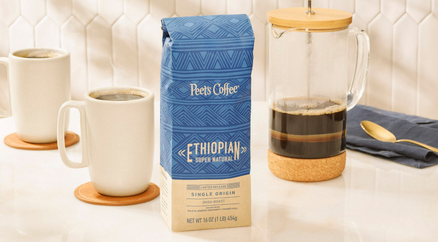 Peet's Coffee Ethiopian Super Natural Coffee Beans in a blue and tan coffee bag, sitting on a counter next to a french press. 