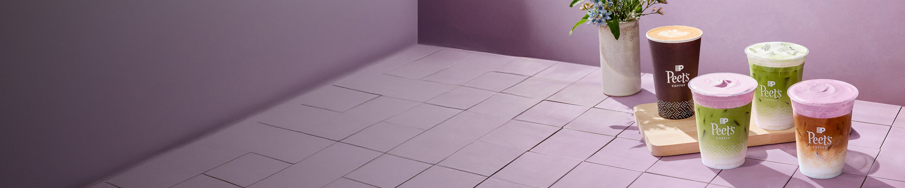 Four coffee cups with lids on a tiled floor, with a purple wall in the background.