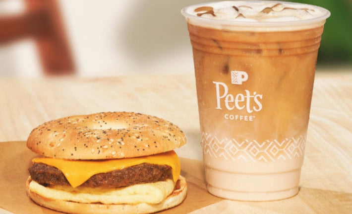 Everything bagel breakfast sandwich with egg, cheese and sausage next to an iced coffee with milk on a countertop