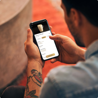 Person holding a smartphone with a coffee ordering app on an orange couch.