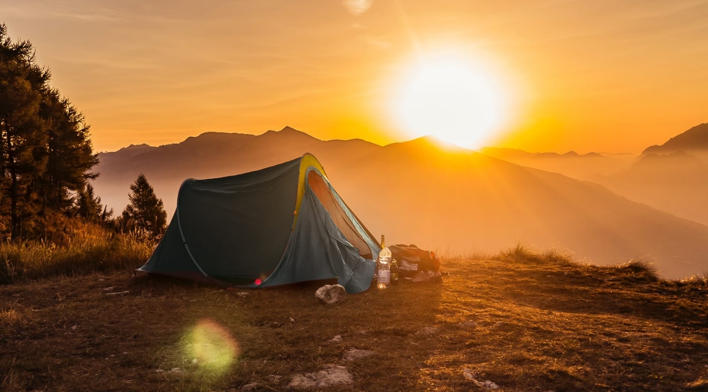 A tent on a peak with the sunrise in the background