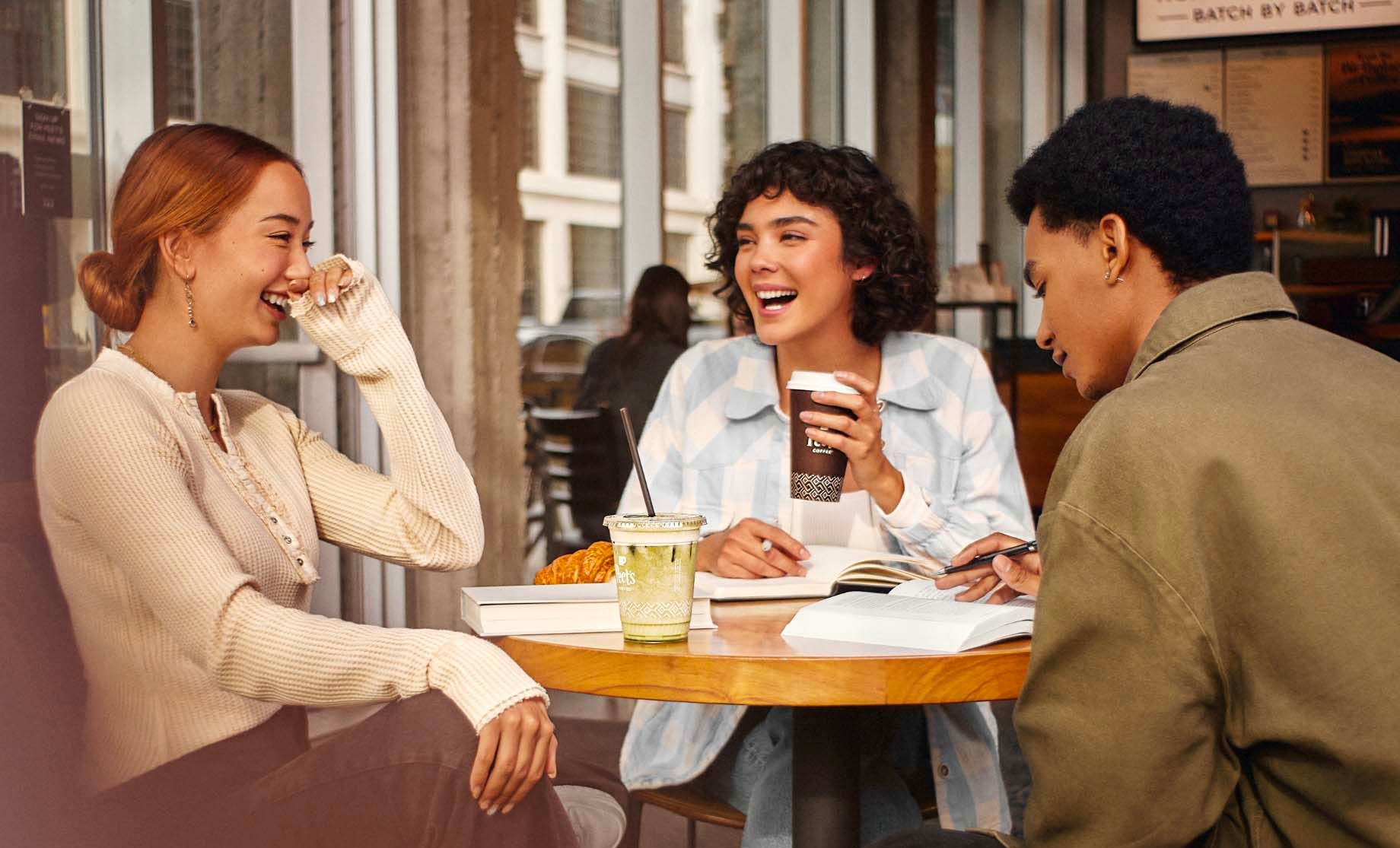 Three people sitting around a table with coffee beverages laughing and reading from open books