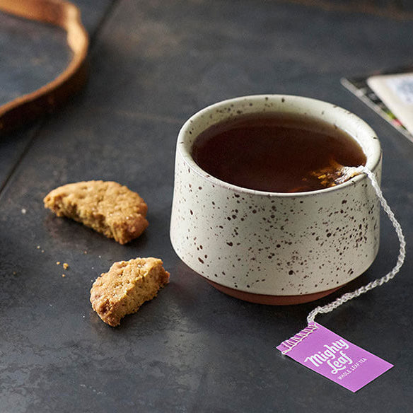 Ceramic mug with tea and cookies on a dark surface