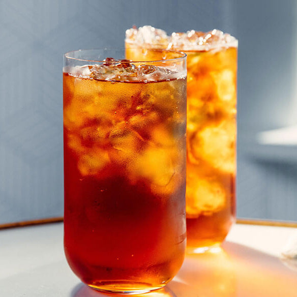 Two glasses of iced tea on a wooden surface with a light blue background