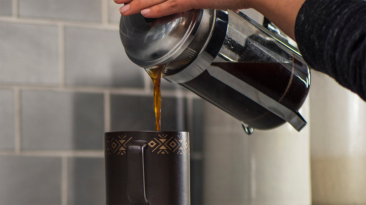 a french press coffee pot pouring coffee into a mug