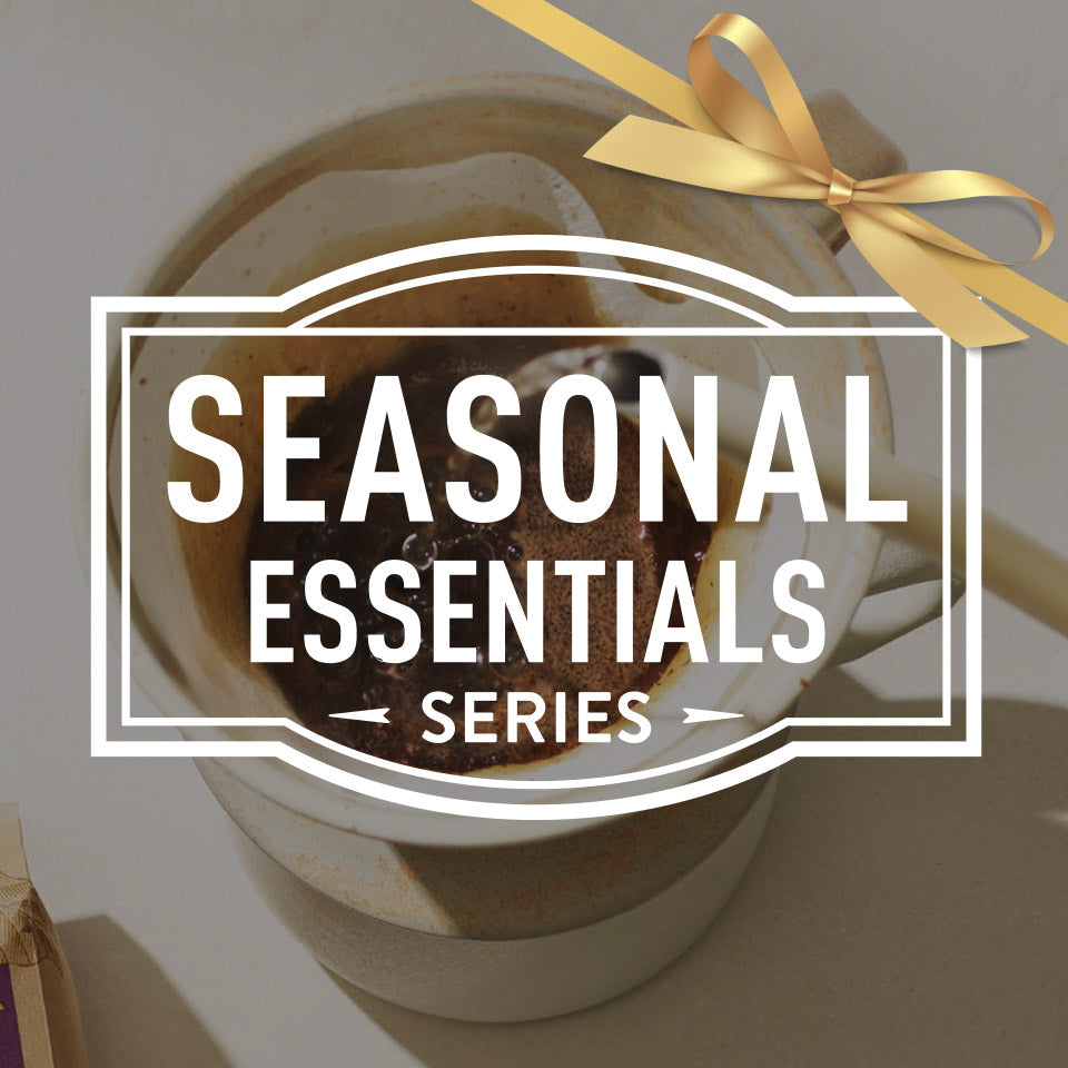 Gift basket with a gold bow labeled 'Seasonal Essentials Series' on a neutral background
